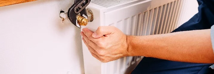 Person montiert Heizkörper mit Rohrzange.